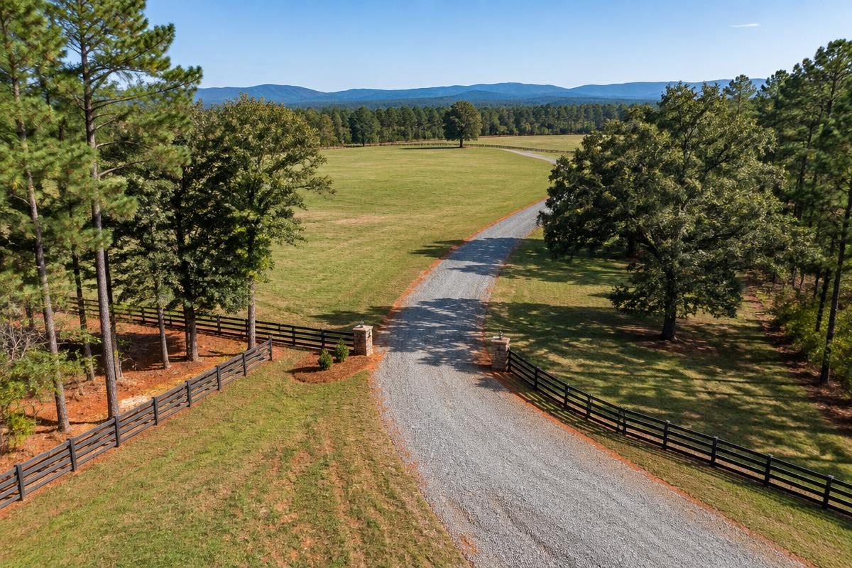 Gravel rural access route across rolling Upstate pasture with distant foothills
